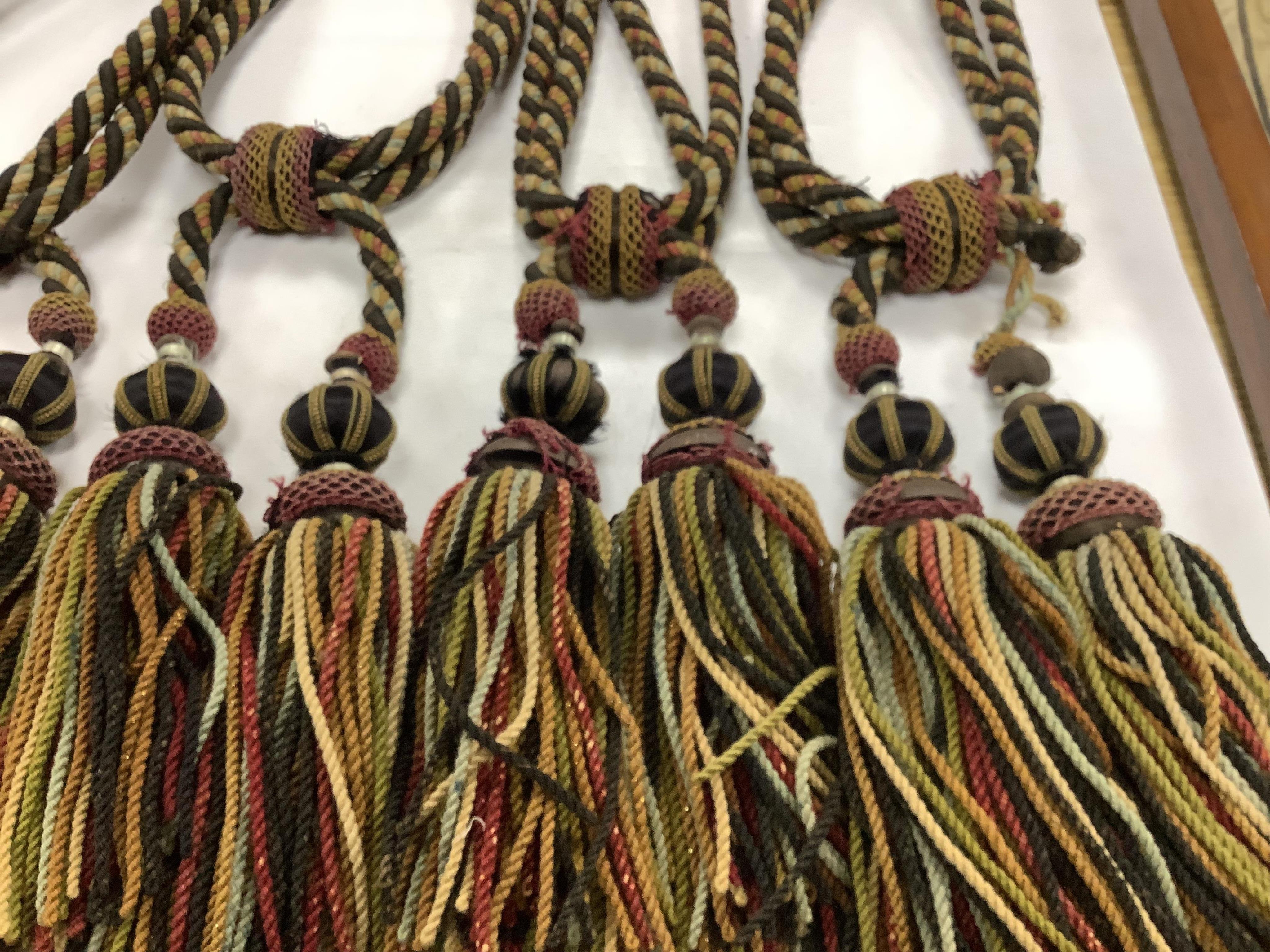 Four pairs of late 19th early 20th century corded and tasseled black and multicoloured tie backs. 69 cm long. Condition - all worn from use and age, one tassel needs repair.
